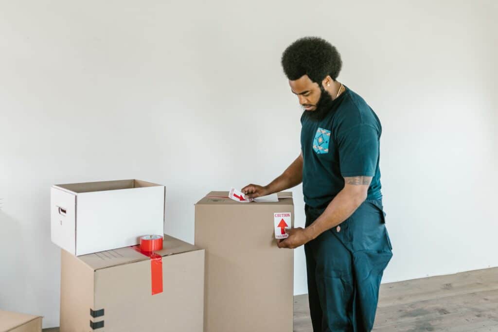 A man preparing cardboard moving boxes with caution stickers in a bright indoor setting