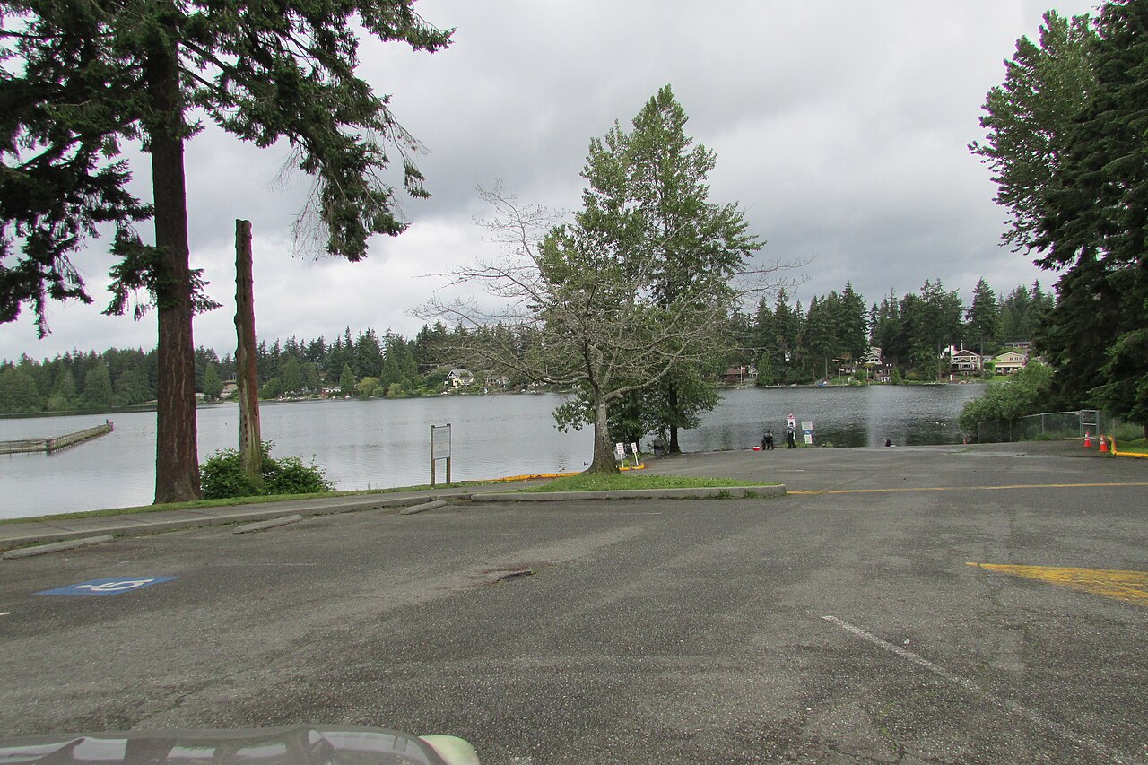 Boat launch and parking area at Steel Lake Park in Federal Way, Washington, with the lake and shoreline homes visible beyond the trees